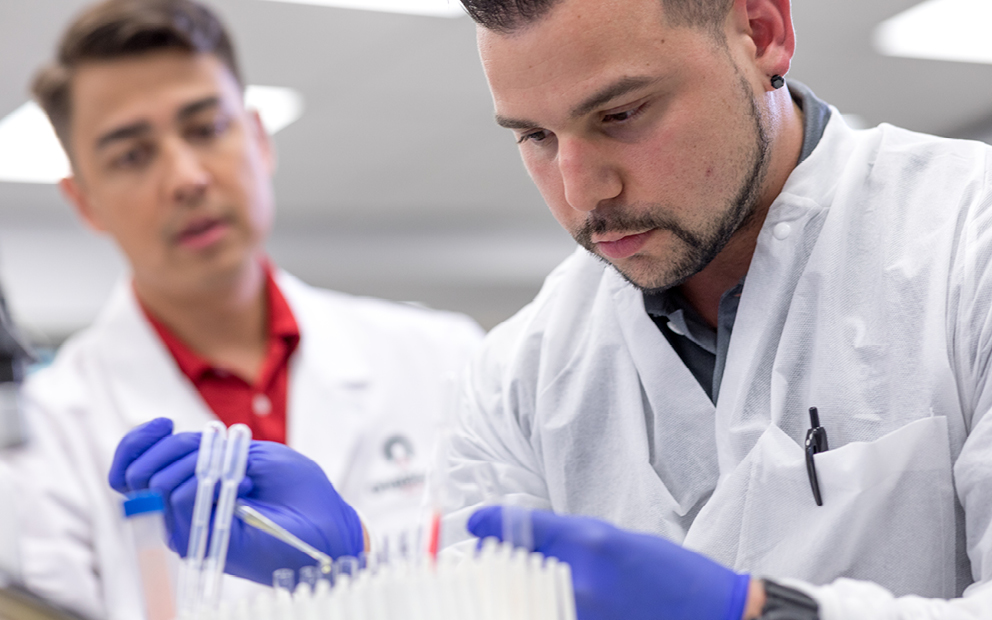 Two men in lab coats looking down at pipette well